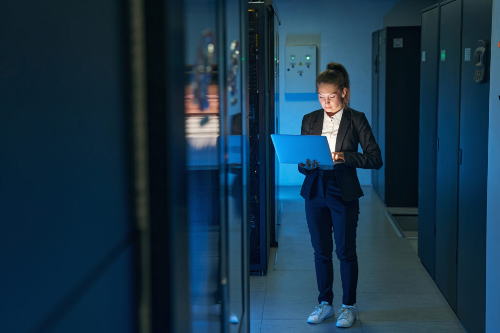 Ejecutiva con laptop en el pasillo de un centro de datos con racks de servidores iluminados en azul
