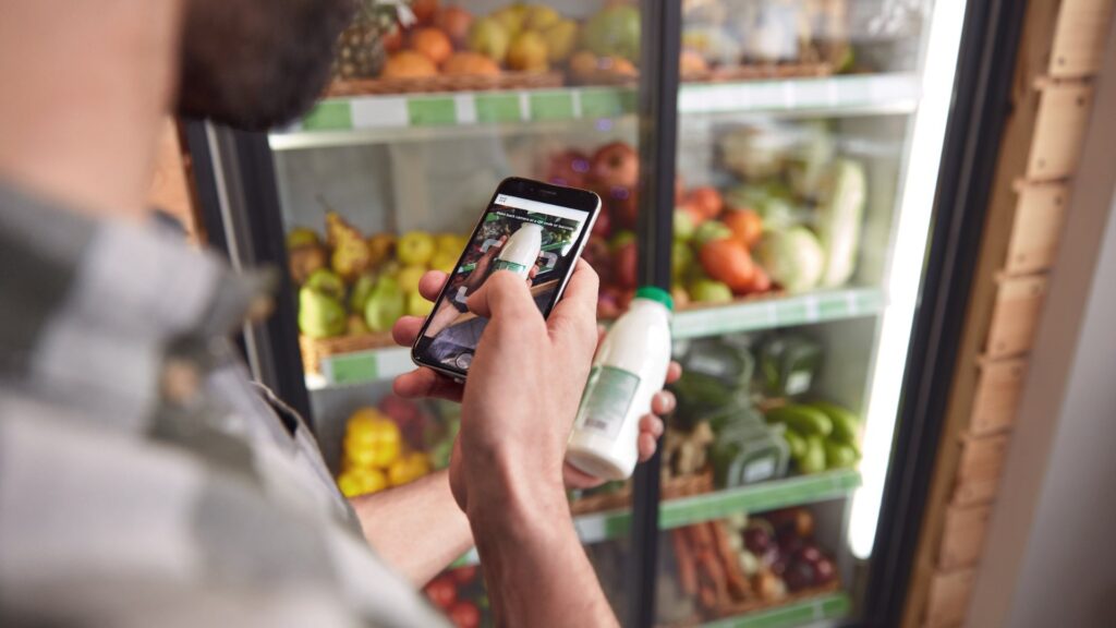 Un comprador escanea con su teléfono la etiqueta de una botella de leche frente al refrigerador de una tienda.